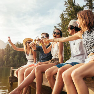 Young friends sitting on a dock toasting beers